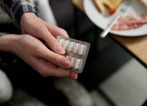 Close-up of a person holding a blister pack of pills with breakfast in the background, indicating medication and daily routine.